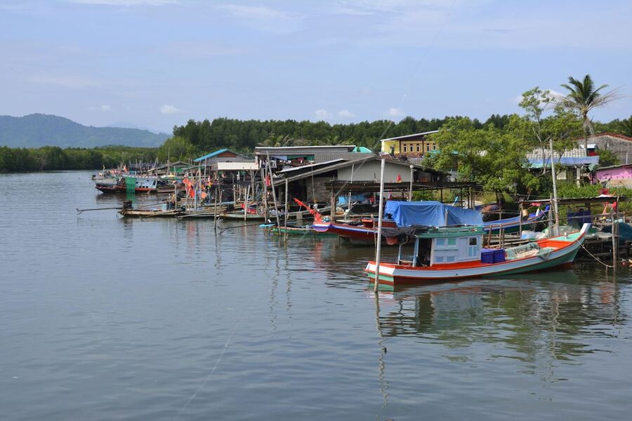 Bateaux de pêche colorés amarrés au village de Khanom, entouré de maisons sur pilotis et d’une nature verdoyante